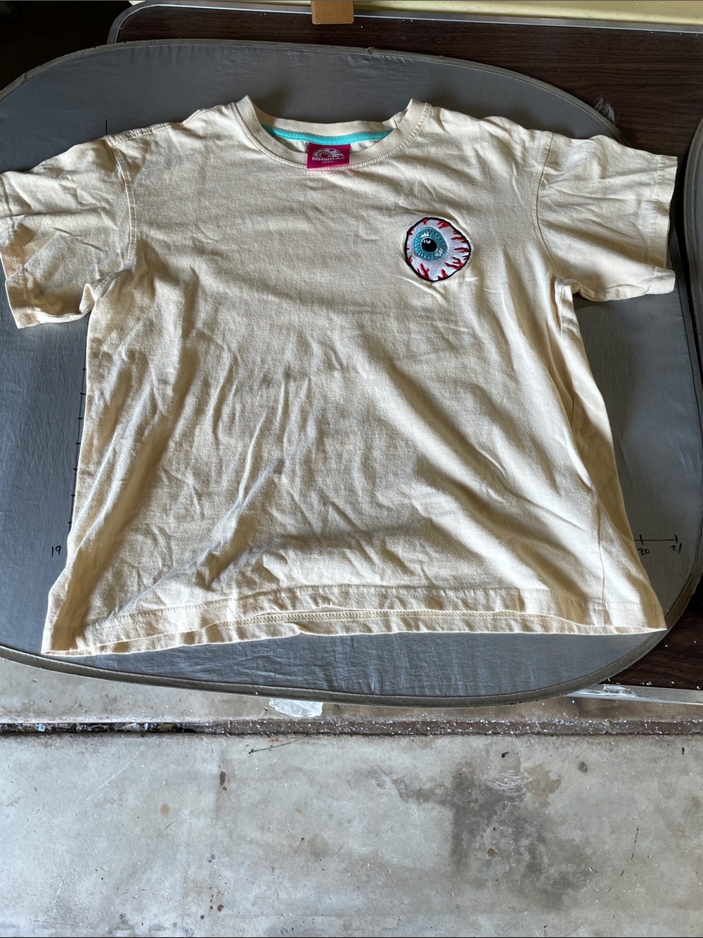 Small Mishka NYC Cream Graphic Tee with Eyeball Patch embroidered pen stain